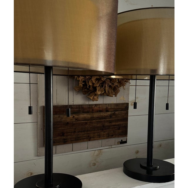 Pair of modern black table lamps with rigid gold molded drum shades and pull-chain switches.