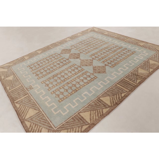 This 8x10 contemporary Art Deco rug showcases a sophisticated geometric pattern in light blue, beige, and earthy brown...
