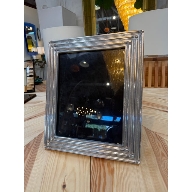 A rectangular picture frame with a polished silver-tone finish and layered, stepped borders. Subtle corner details add...