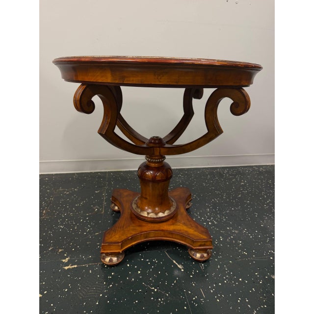 Elegant vintage round center table featuring burl wood veneer, a decorative inlaid top, and a Regency-style pedestal base....
