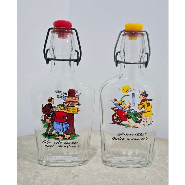 Vintage German swing‑top liquor bottles featuring colorful cartoon scenes and cheeky German phrases make a playful...