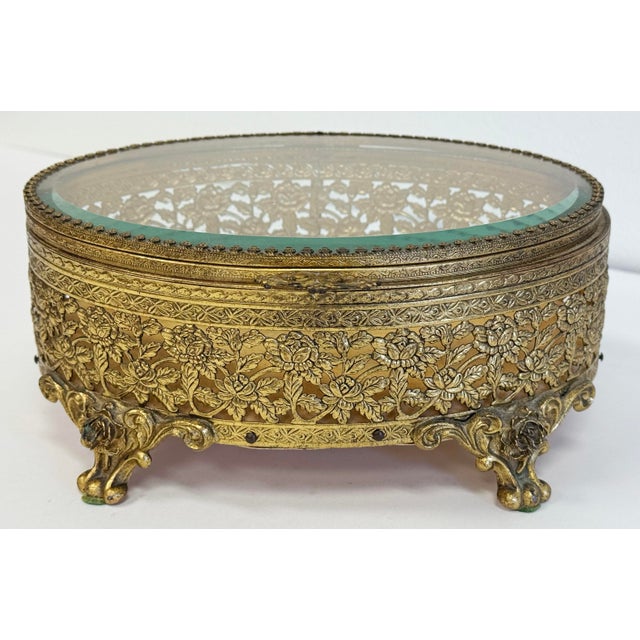 Vintage gilded brass Ormolu jewelry box with beveled glass top with a gold velvet lining to interior. Frame features...