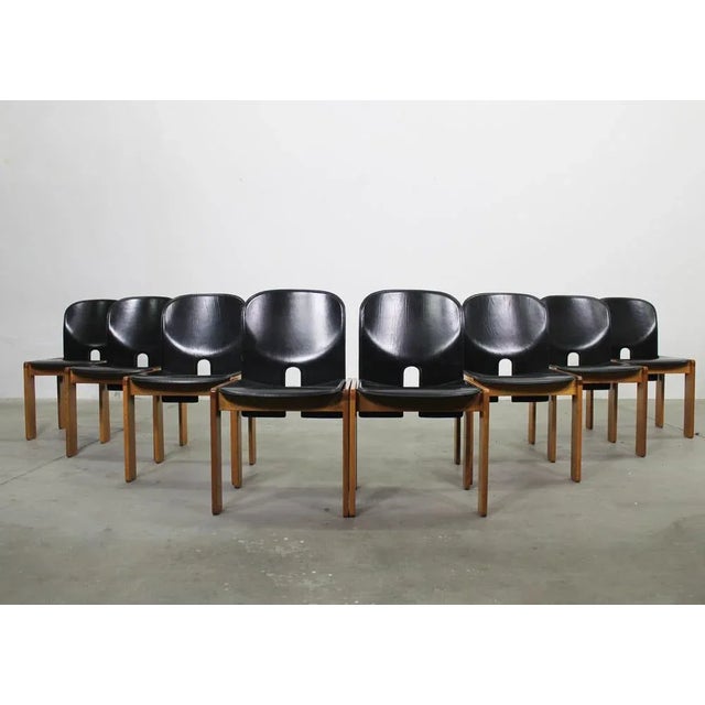 Set of eight 121 chairs with structure in wood, seat and back in foam rubber padding covered with black leather. Designed...