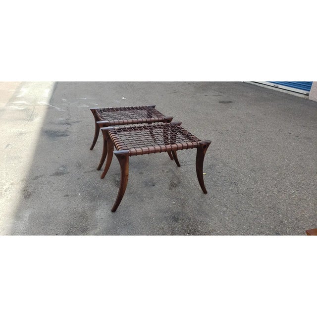 Pair of Robsjohn Gibbings style ottomans. The ottomans are in good condition. The wood has a walnut stain. Leather cording...