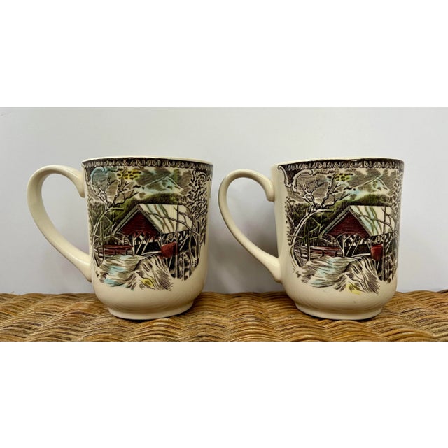 A set of two coffee mugs in traditional transferware- They each feature alike the "Covered Bridge" scene in the Friendly...