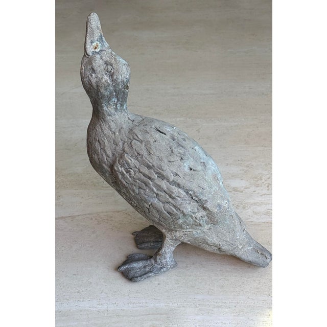 A cast zinc duck with head raised and beak lifted, finely detailed with layered feather texture and webbed feet....