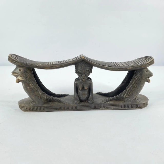A carved double headrest from the Songye people is a sculptural sleeping support traditionally used in the savanna regions...