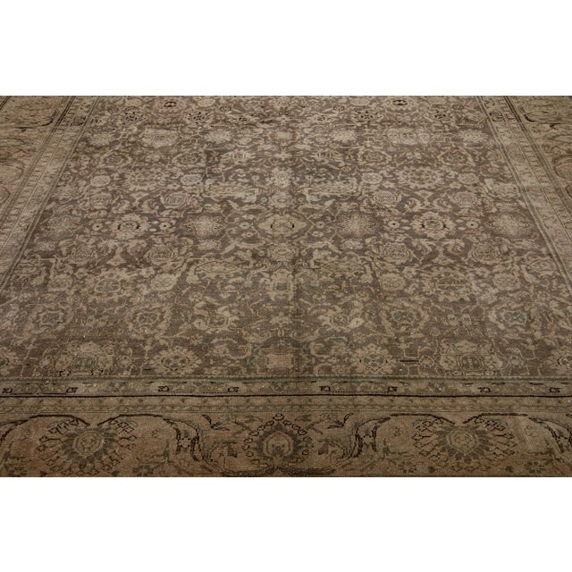 This antique Tabriz rug boasts a brown color field and features exquisite, hand-knotted wool construction complemented by...