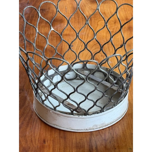 Old wire basket with looped sides and a solid metal bottom. Worn finish with a simple, sturdy look.