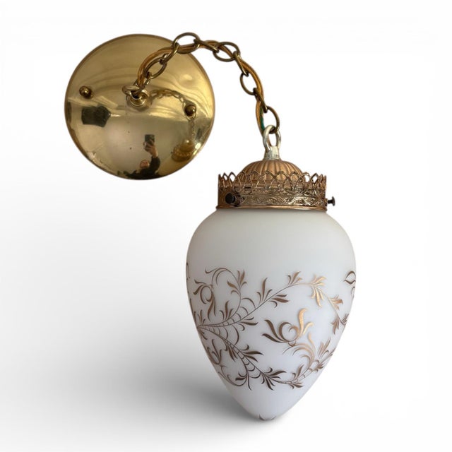 Gorgeous pair of pendent lights featuring frosted glass shades adorned with scrolling gold patterns and topped with...