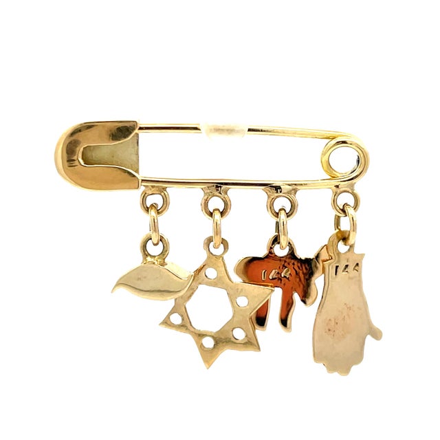 Elegant 14K yellow gold brooch featuring a safety pin design adorned with five symbolic charms: a hand, a butterfly, a...