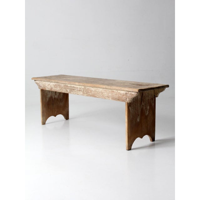 This antique wood bench features a long plank seat with gently shaped ends and a time-worn painted surface that has...