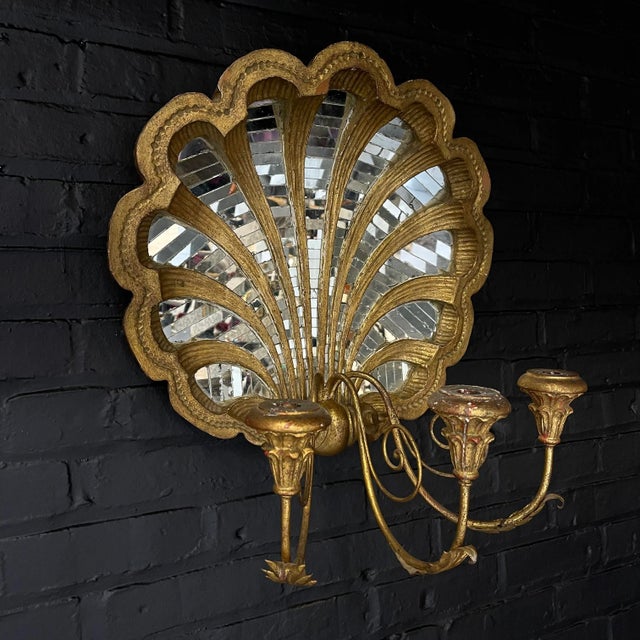A gilt carved mirror in the shape of a shell with mirror mosaic tiles and with a three arm sconce with three candle...