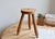 This raw wood tripod stool charms with its simple and authentic form, featuring a thick, round seat and three slightly...