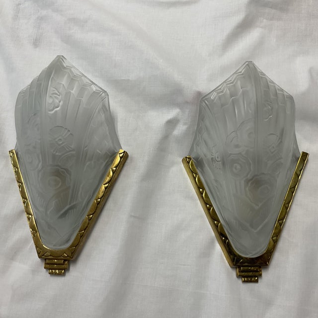 Elegant pair of decorative wall sconces featuring sculptural frosted glass shades set with gilt brass frames. Each molded...