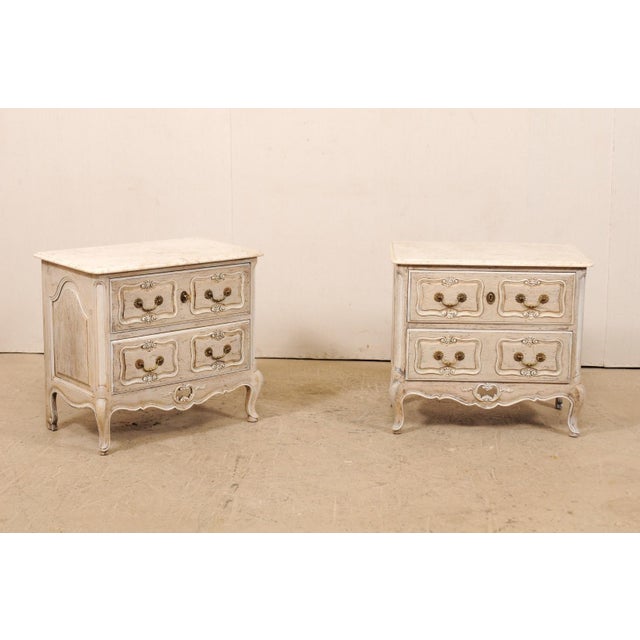 A pair of French two-drawer side chests with marble tops from the mid 20th century. This pair of vintage commodes from...