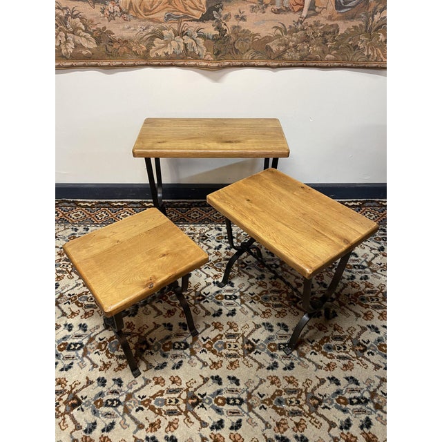 A stylish set of three vintage industrial nesting tables, each featuring a sturdy wrought iron base paired with plain oak...