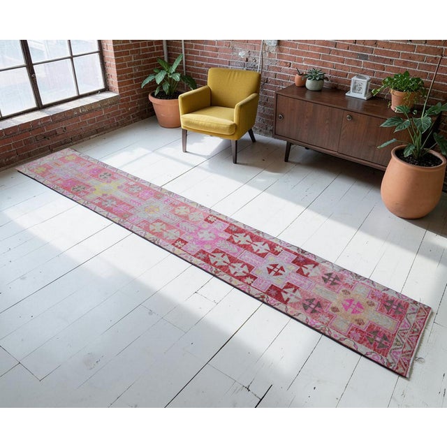 This authentic 1960s Southeastern Anatolian runner rug features a vibrant tribal geometric design in magenta pinks and...