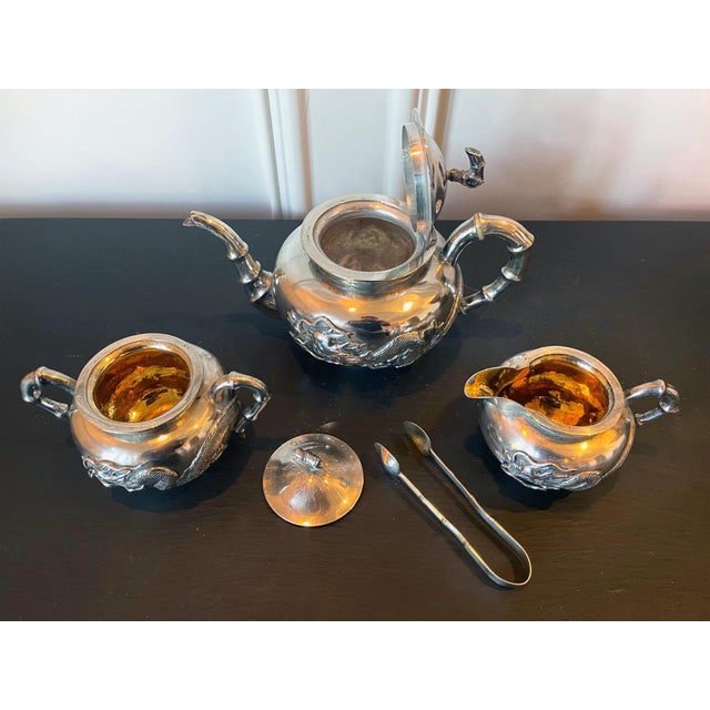 A four piece Chinese export silver tea service set consists of a lidded teapot, a creamer with lid, an open sugar and a...