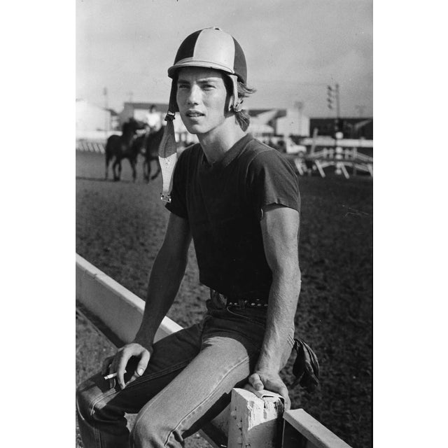 1983 black & white photograph of jockey Bobby Walker sitting on a fence. Article and publication information is on the back.