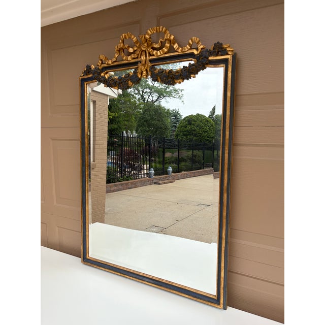 An elegant Italian giltwood mirror featuring carved floral swags, ribbon cresting, and a beautifully muted blue painted...