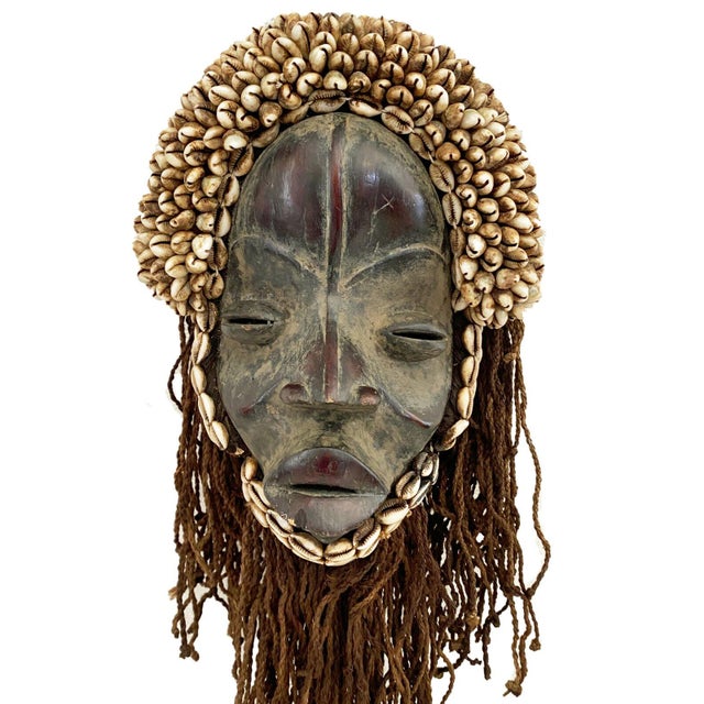 This magnificent Vintage Dan Mask features Deangle Cowry Shells on a custom iron stand. It is a ceremonial dance mask from...