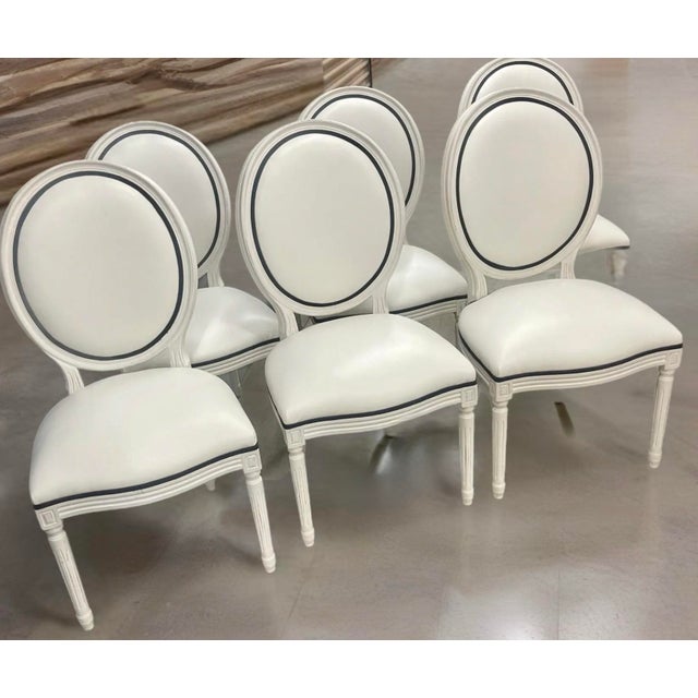 A chic set of 6 Louis XVI style balloon back dining chairs, recently upholstered in white leather with black welting. The...