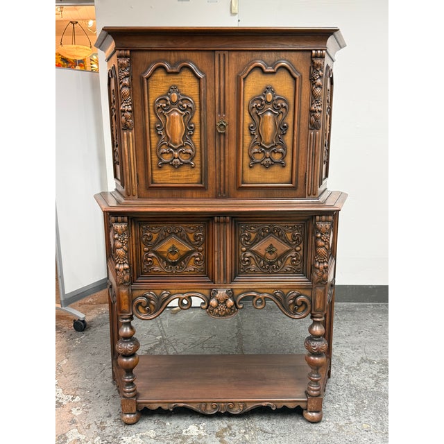 Design Plus Gallery presents a 1920's Tudor Revival Carved Walnut Highboard Cabinet by Empire Manufacturing Company. This...