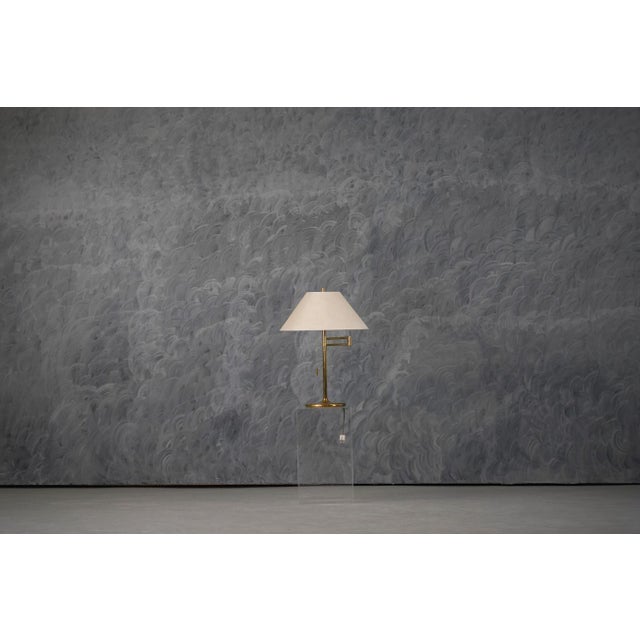 A vintage table lamp produced in Germany during the 1970s, crafted in polished gold-colored metal with a fabric lampshade....