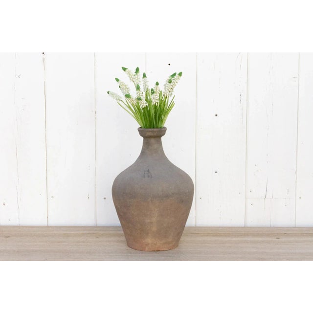Showing a charming oxidized gray finish, this amphora pottery vase has a rounded shape with texture and a narrow neck....