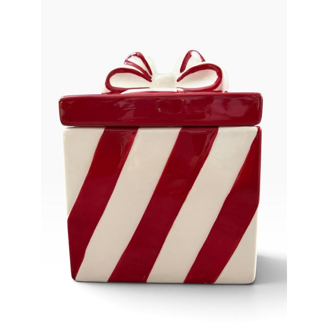 Whimsical vintage Savino Designs cookie jar designed as a wrapped gift box, featuring bold red and white striping and a...