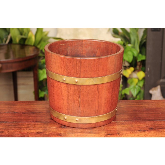 An English Edwardian period R.A Lister & Co. oak bucket with brass braces. This charming English Edwardian period oak...