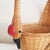 A vintage wicker duck motif basket with a tall handle. This whimsical basket features a handle woven with a wooden duck or...