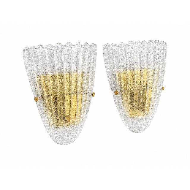 An elegant pair of Murano glass wall lamps, featuring a refined fan shape with a hammered surface and vertical grooves...