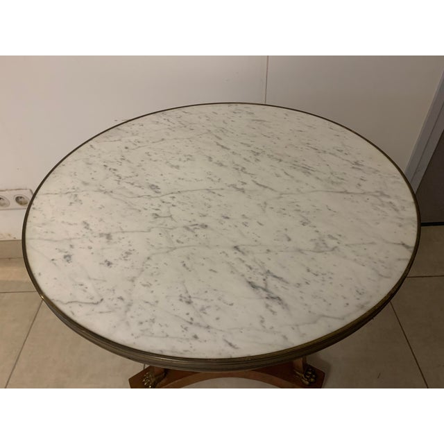 Round Empire-style pedestal table Tripod base with a crotch shelf White veined Carrara marble top Marble with a brass...