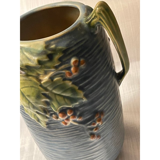This vintage Roseville Pottery BUSHBERRY Blue 31-7 Double Handled Art Deco Vase is a vintage piece from 1941, showcasing a...