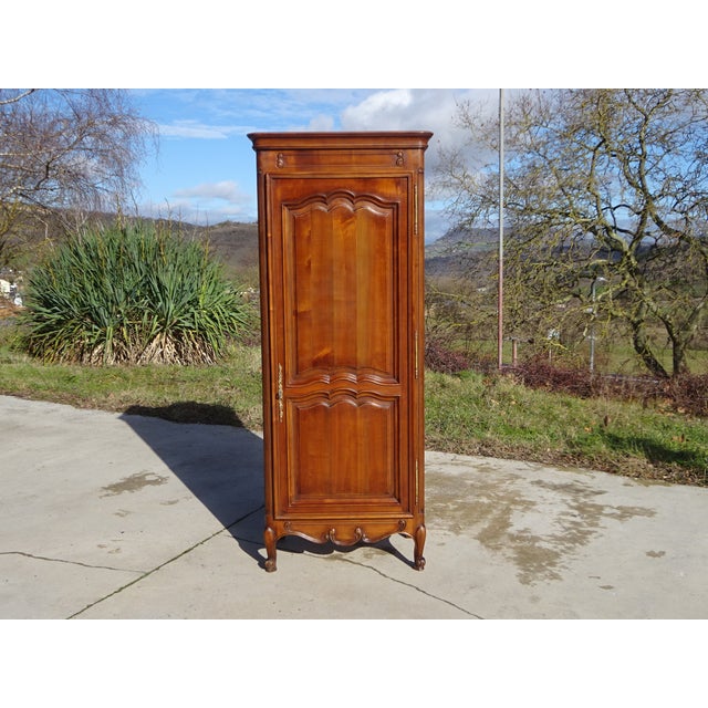 A bonnetière (wardrobe) crafted entirely from solid cherry wood, traditionally made in France in the 1980s. This tall,...