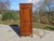 A bonnetière (wardrobe) crafted entirely from solid cherry wood, traditionally made in France in the 1980s. This tall,...