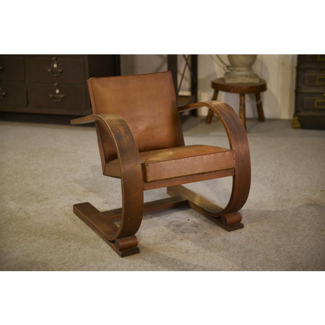 A low armchair from the 1950s, with a highly sculptural design, featuring wide, curved wooden armrests that form a...