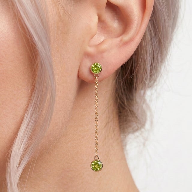 The earrings are adorned with vibrant, round-cut natural peridot gemstones that offer a lively, fresh lime-green hue. The...