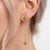 The earrings are adorned with vibrant, round-cut natural peridot gemstones that offer a lively, fresh lime-green hue. The...