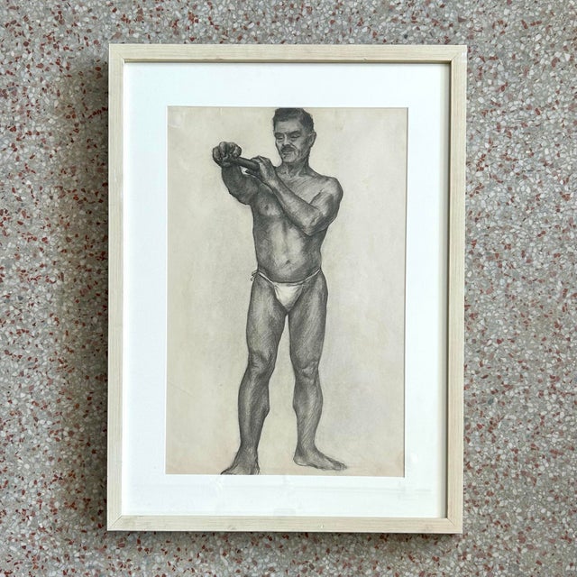 This framed charcoal drawing features a detailed study of a male figure in a natural pose, rendered with strong anatomical...