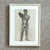 This framed charcoal drawing features a detailed study of a male figure in a natural pose, rendered with strong anatomical...