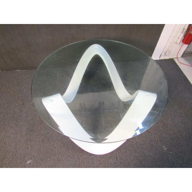 Unique glass table featuring a flowing white base on three contact points. The top is round and has an elegant beveled glass.