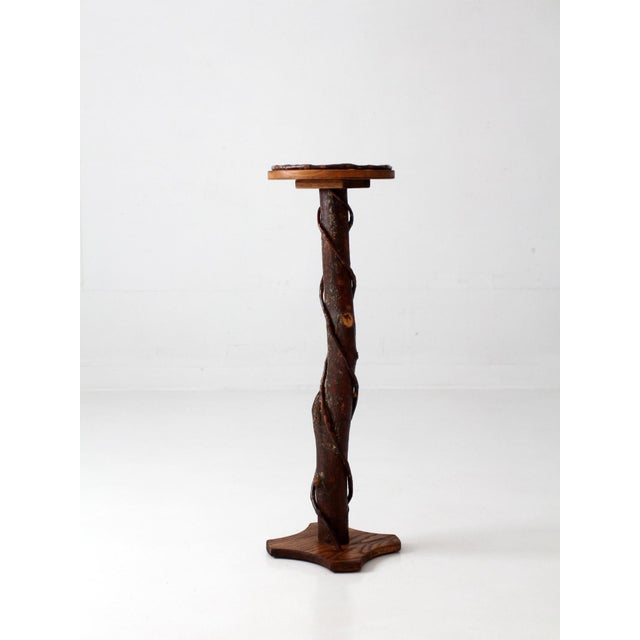 Rustic Adirondack plant stand featuring a natural twig pedestal wrapped with winding vine details and topped with a round...