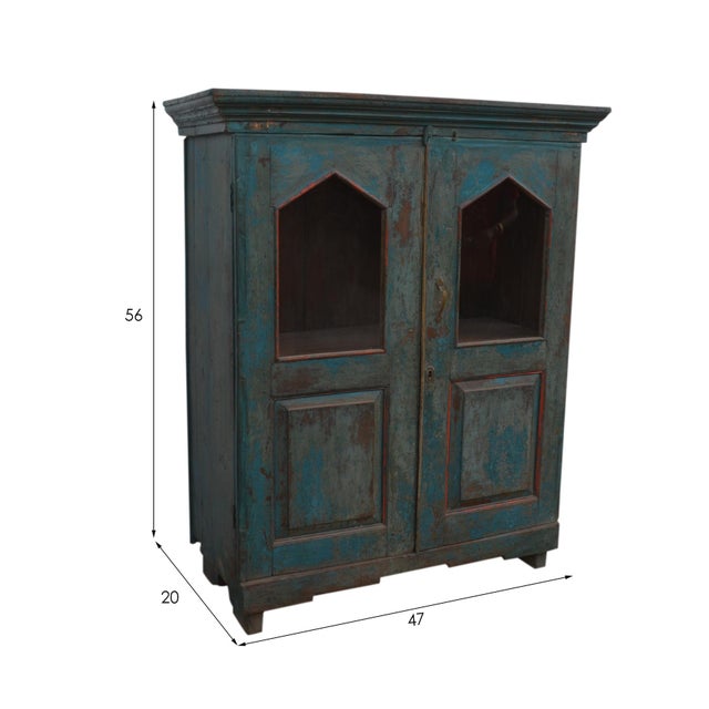 This reclaimed teak wood glass fronted cabinet features a solid rectangular design with a blue color and aged metal...