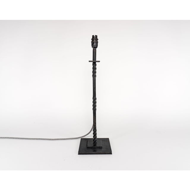 A tall, slender hand-wrought iron table lamp with a heavy two-step plate base and a stem with three twists along its...