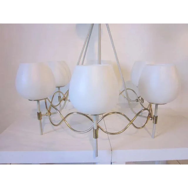 A Mid-Century chandelier with six white globes sitting on wave-like sinusoid- sphere brass metalwork with radiating...