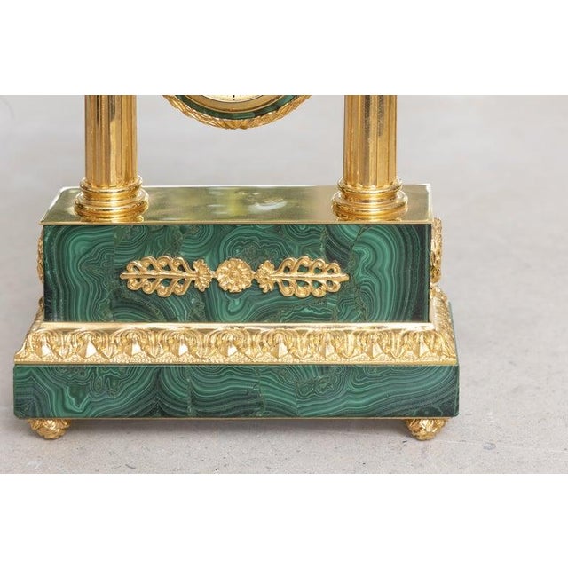 This is a striking Russian Empire-style portico mantel clock, richly veneered in vibrant green malachite and adorned with...