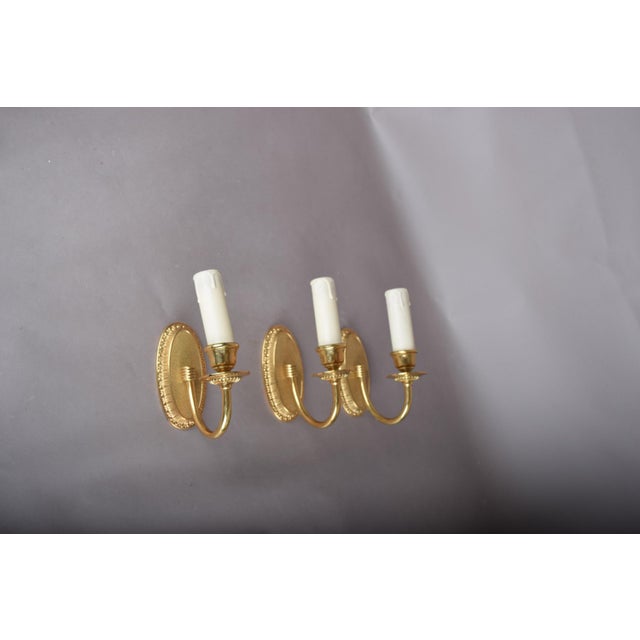 Set of three matching 1950s single-arm wall sconces in the Louis XVI style. Each solid gilt-metal sconce has an oval...